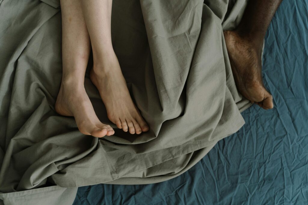 Close-up of an intimate couple's feet entwined on a bed, symbolizing comfort and togetherness.